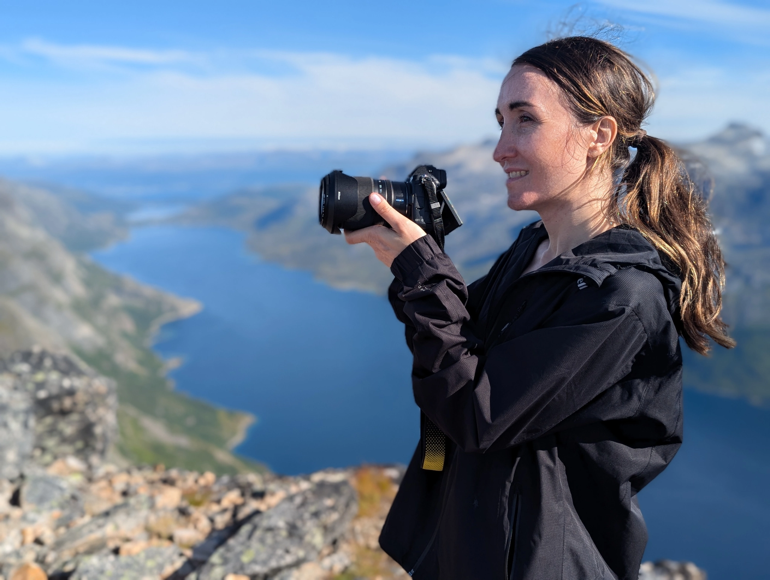 Elizaveta Vereykina standing on a mountain above a fjord holding a camera